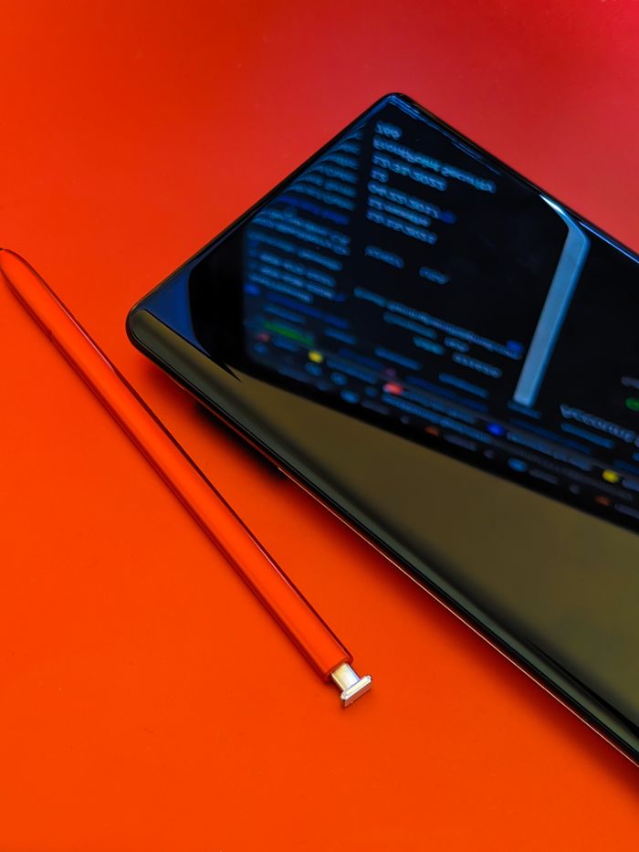 A close-up view of a smartphone with a stylus resting on a vivid red surface, highlighting contemporary technology.